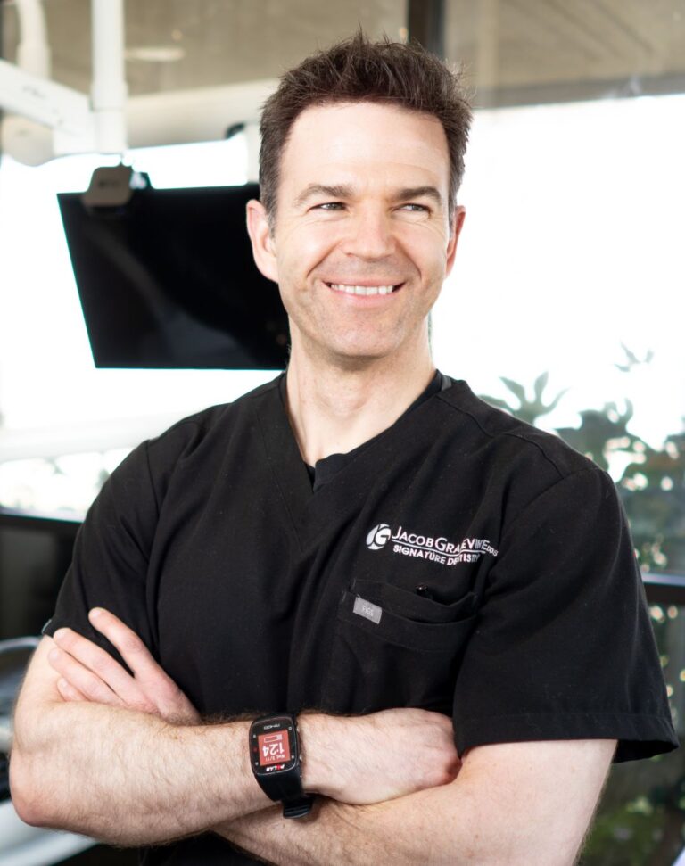 Smiling man in black medical scrubs with arms crossed.