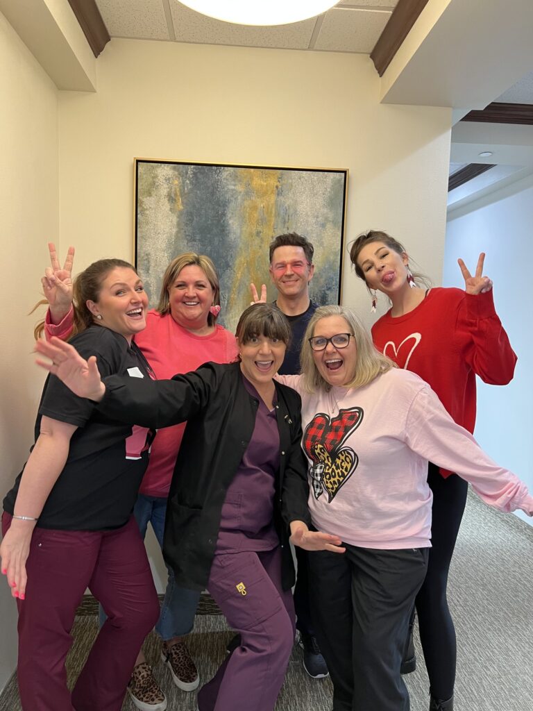 A group of six people posing happily indoors, making peace signs.