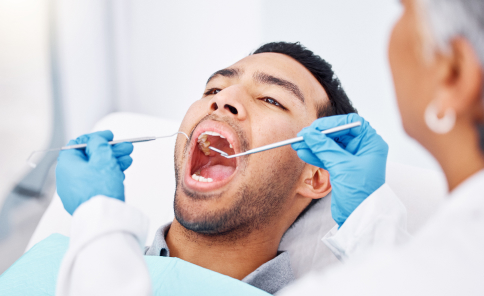 A man undergoing a dental checkup with a dentist's tools.