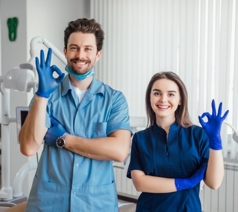 Two dental professionals smiling with gloves and a mask.